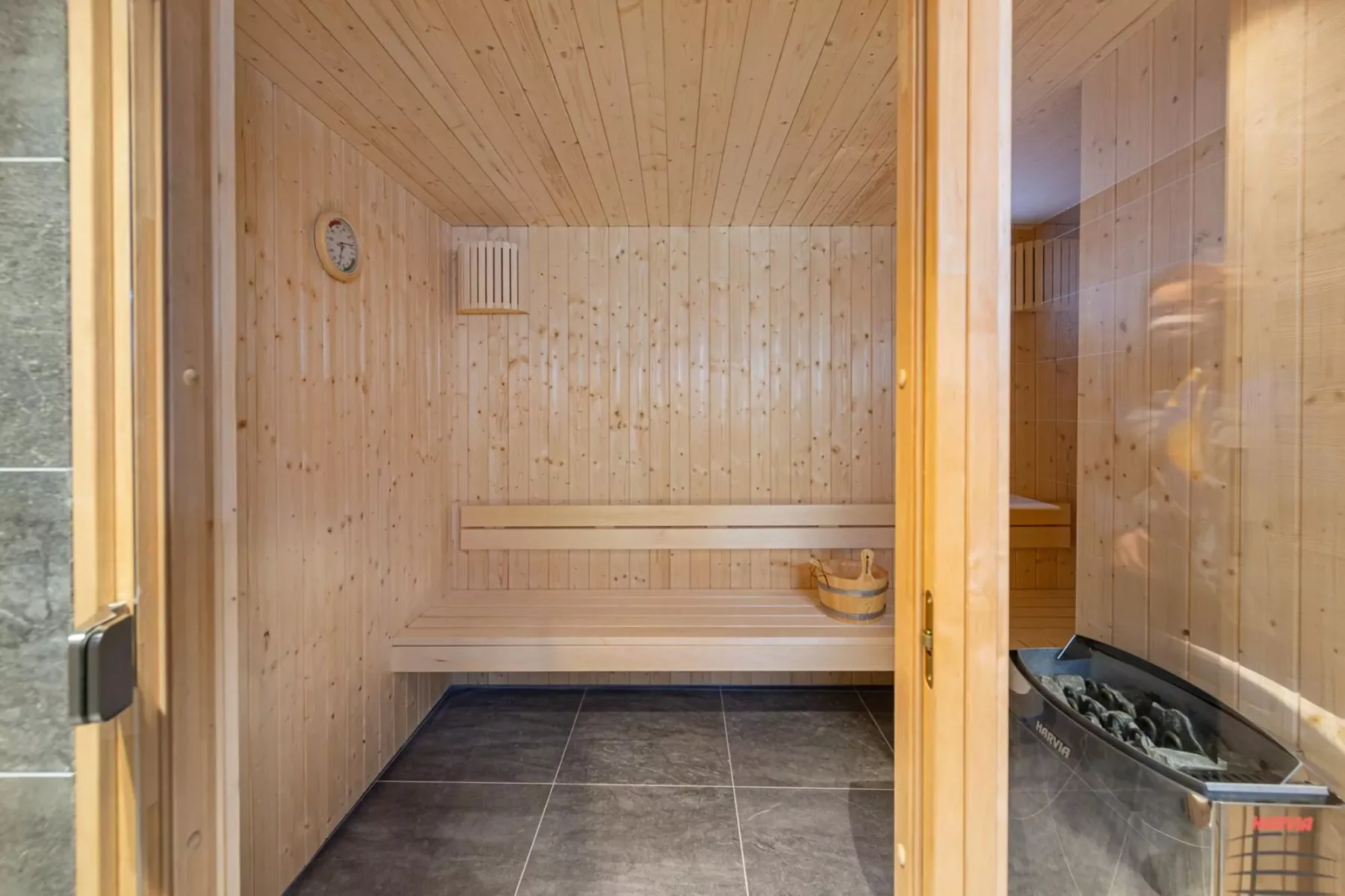 A wooden sauna room with tiered seating and a heater.