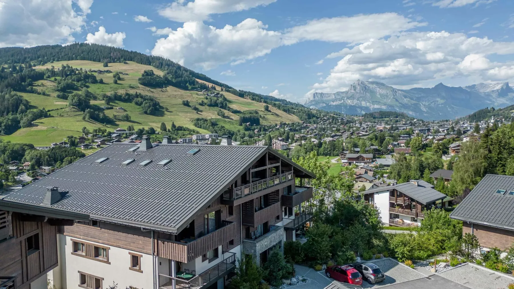 A hillside village with buildings, green slopes, and mountain peaks in the distance.