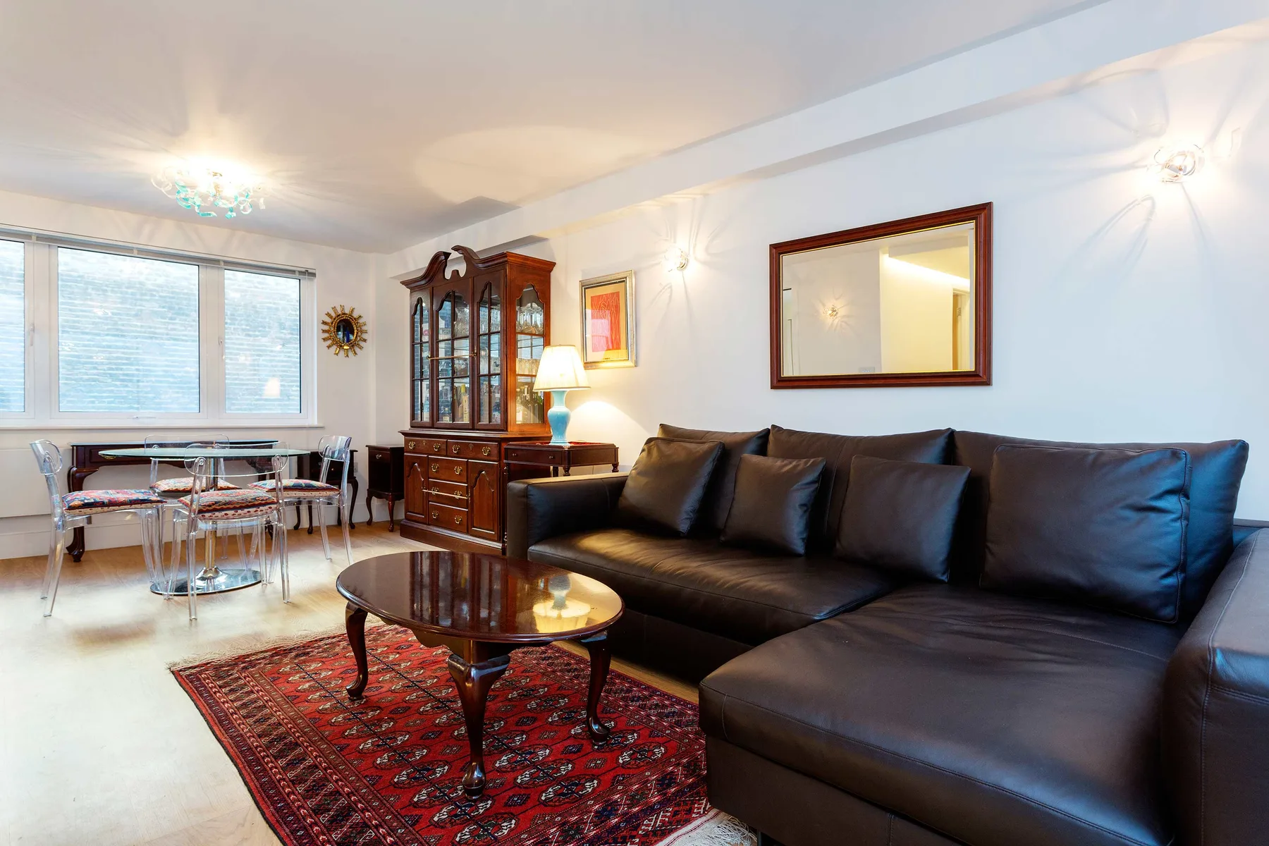 Una sala de estar con asientos oscuros, una mesa de centro y un comedor junto a las ventanas.