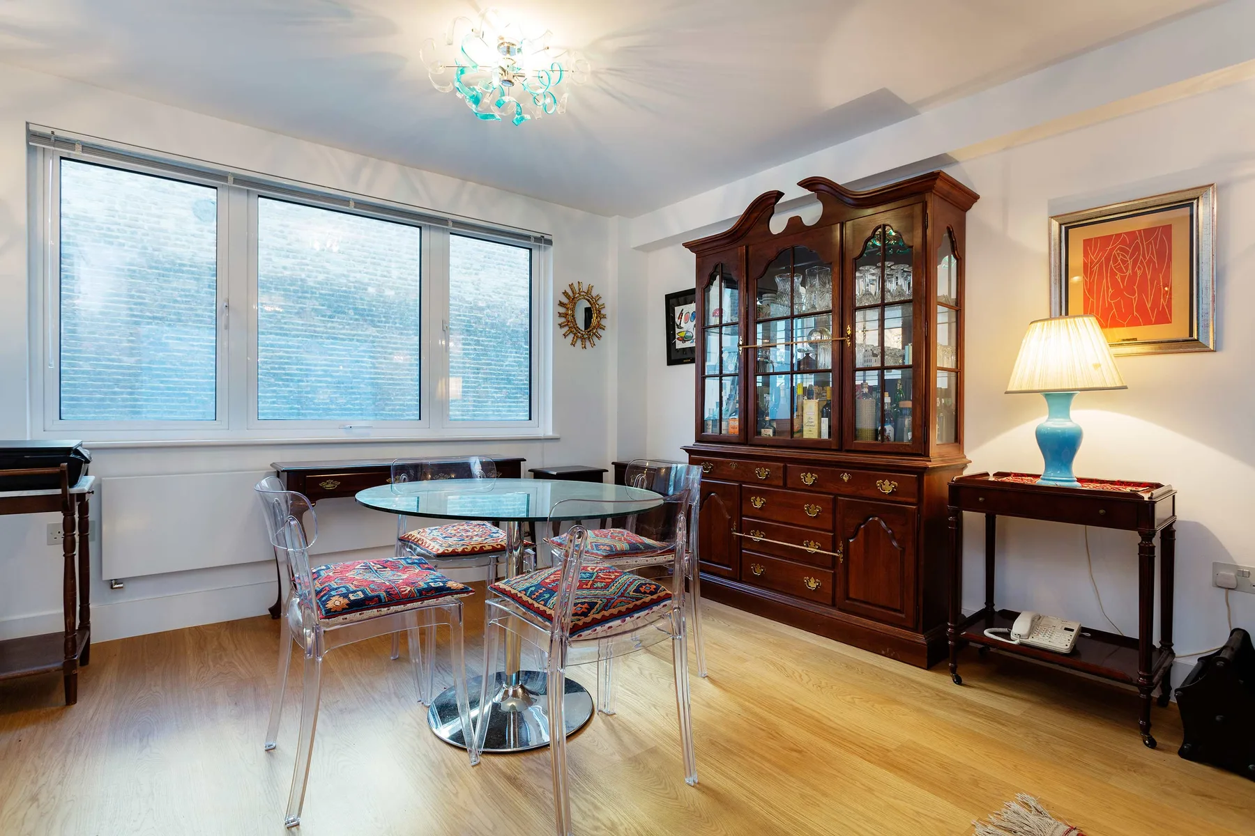 Un comedor con una mesa de vidrio, asientos y un gran mueble de madera.