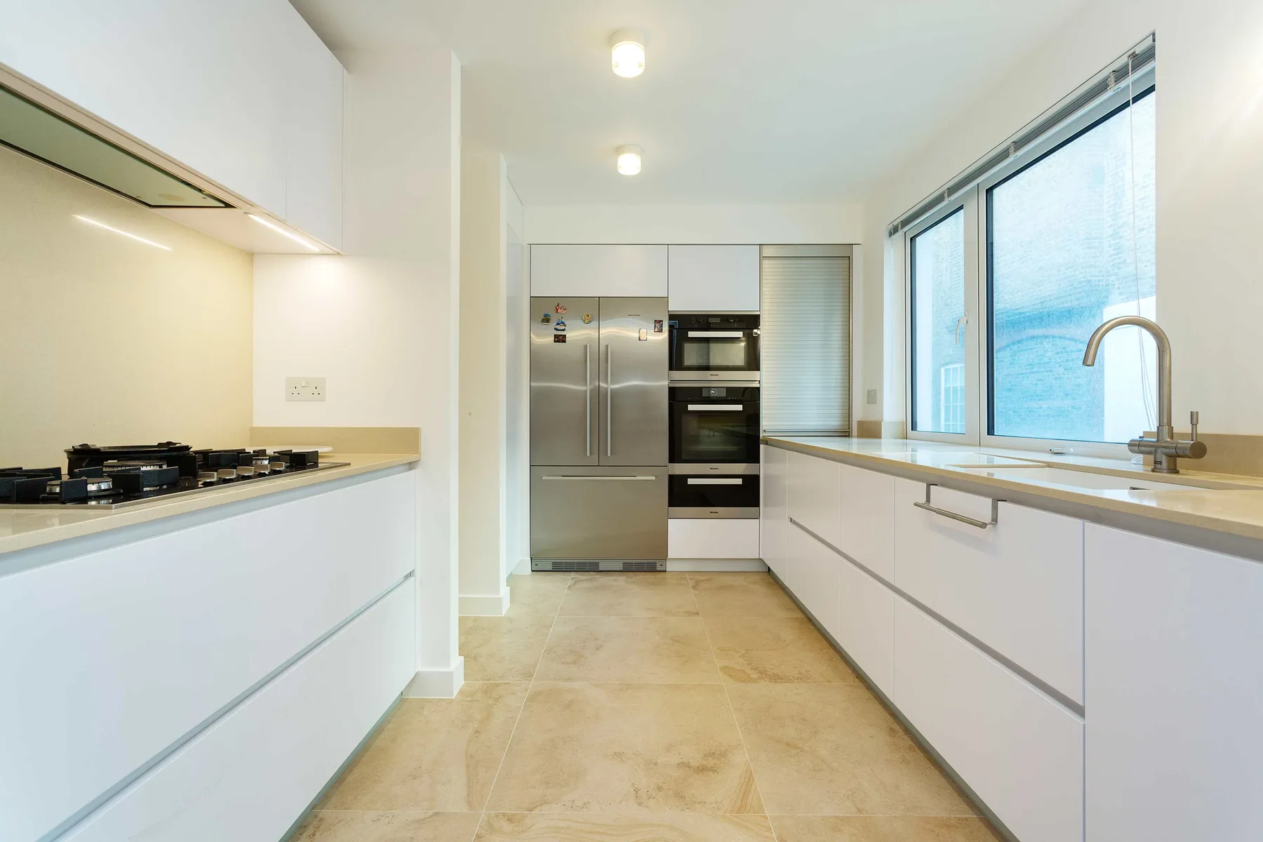 Una cocina moderna con electrodomésticos integrados, gabinetes claros y una encimera junto a grandes ventanas.