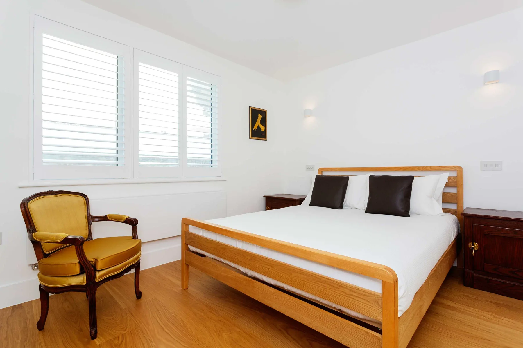 Un dormitorio luminoso con una cama de madera y un sillón amarillo tapizado.