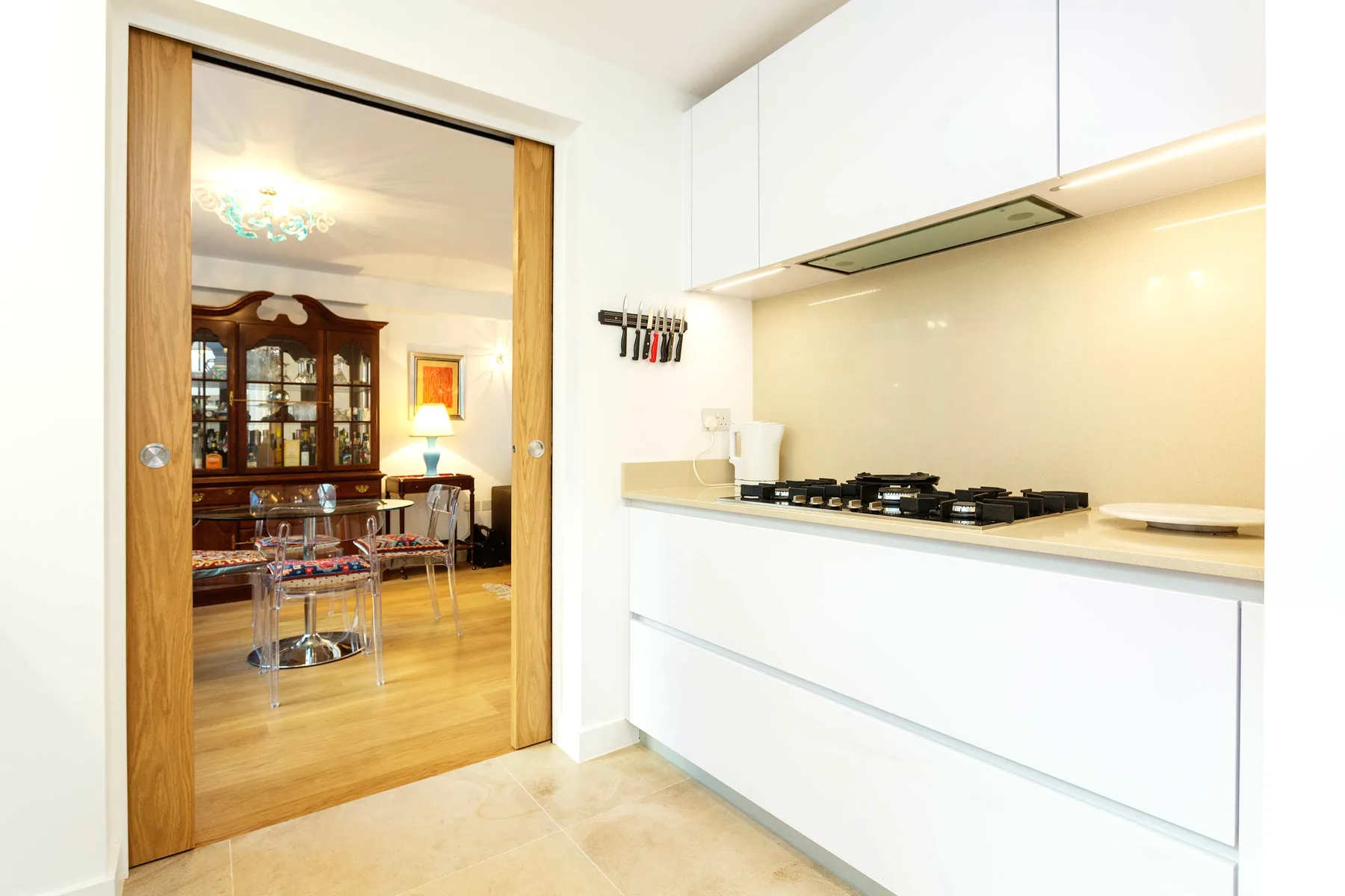 Una cocina moderna con gabinetes blancos y una estufa en la encimera se abre a un comedor.