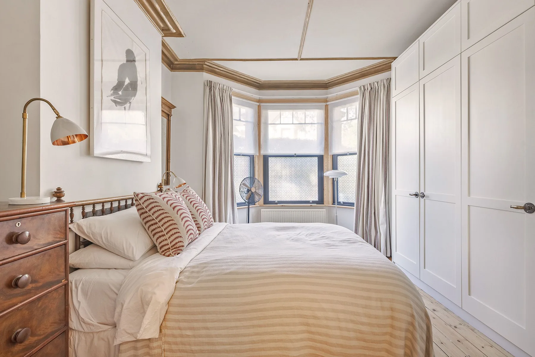 A bright bedroom with a large bed and tall white built-in cupboards.