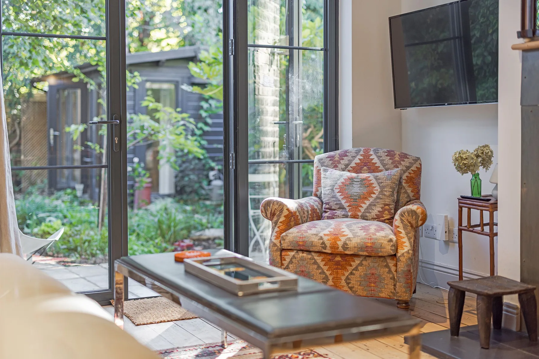 A living room with a patterned armchair and large glass doors opening onto a garden.