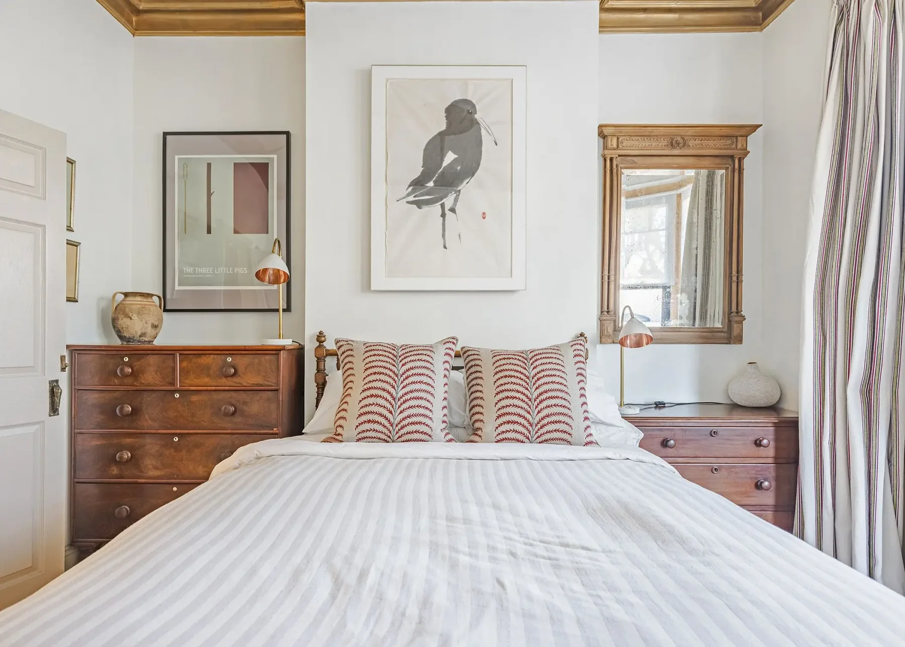A bedroom with a neatly made bed, patterned pillows, and wooden dressers.