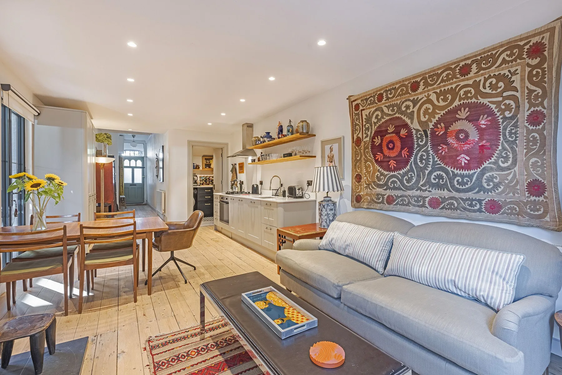 Una sala luminosa con asientos, una mesa de comedor y una cocina al fondo.