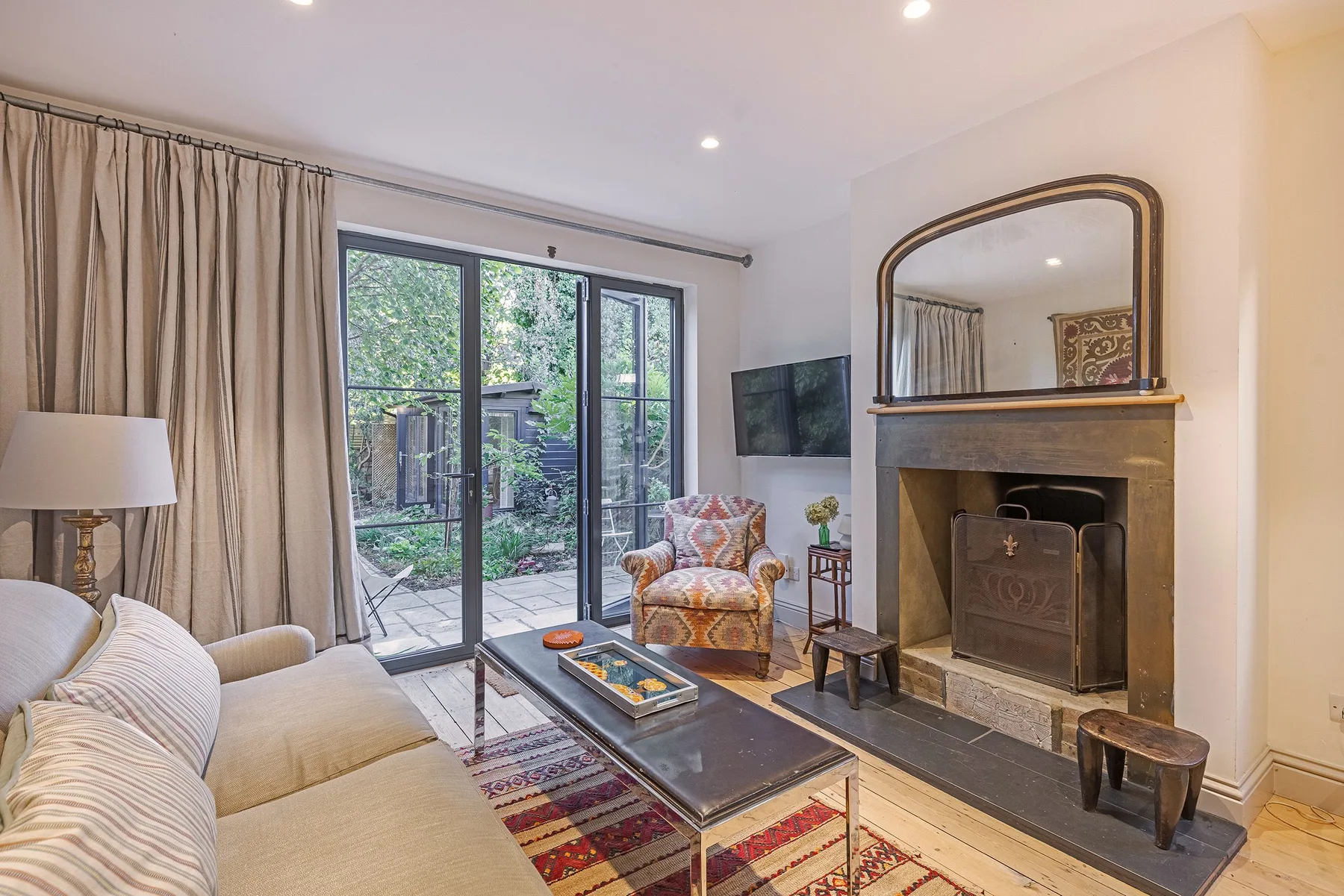 Una sala de estar con asientos, una chimenea y puertas de vidrio hacia un jardín.