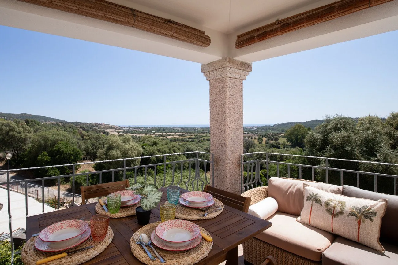 A covered outdoor terrace with dining seating and a view of green hills.