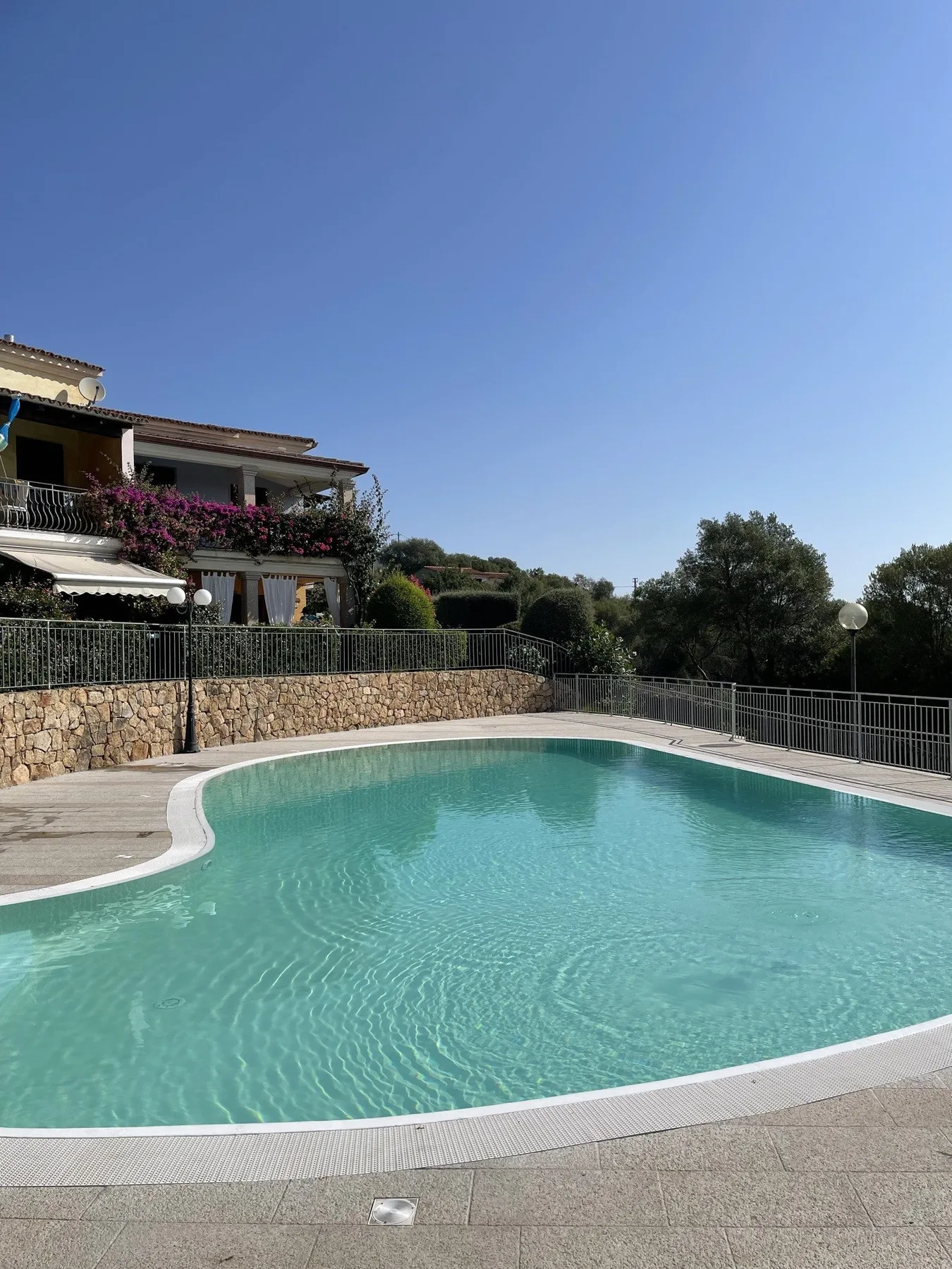 A swimming pool with a curved edge sits beside a fenced outdoor area.