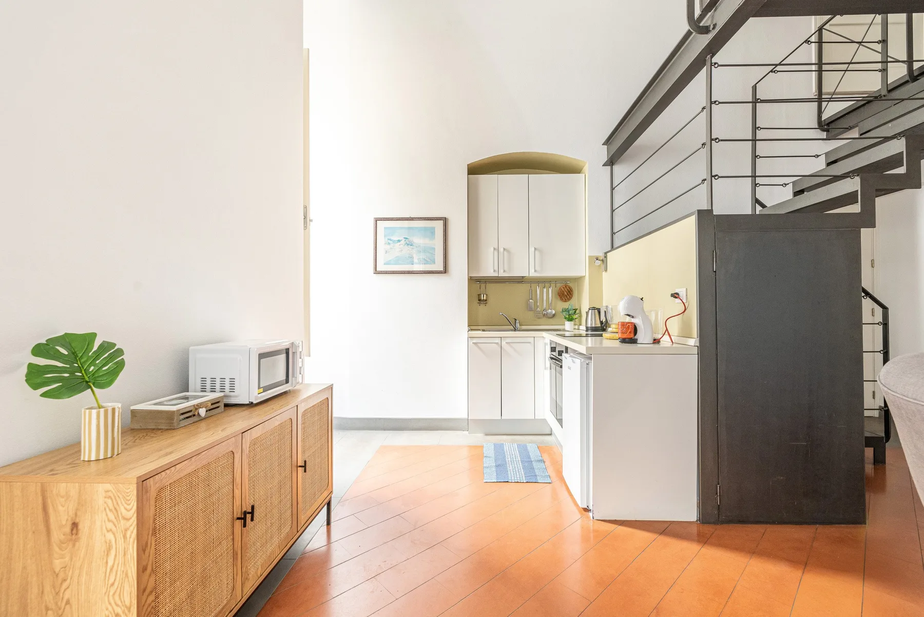 Una luminosa sala de estar abierta a la cocina, con un aparador de madera bajo una escalera.