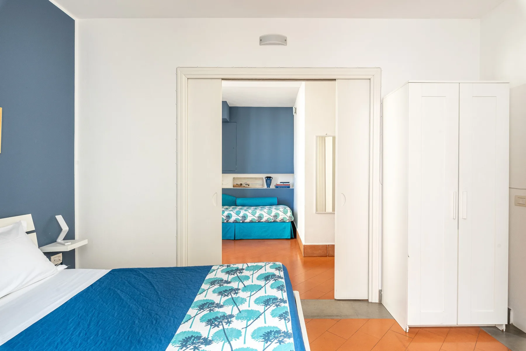 Un dormitorio con una colcha azul y un armario blanco.