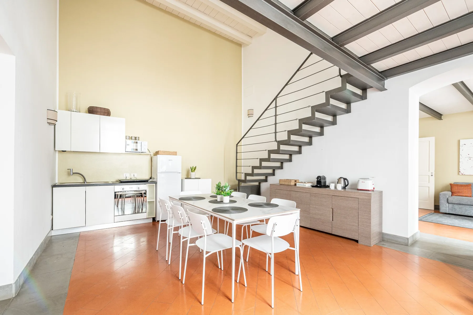Una cocina abierta con comedor y una mesa bajo una escalera.
