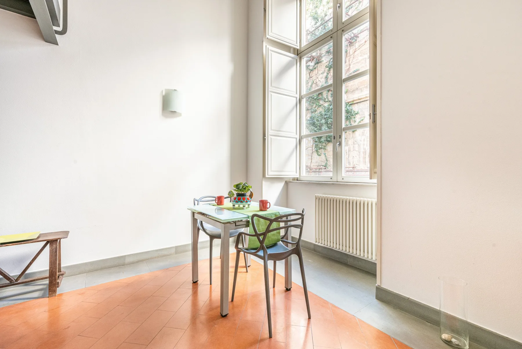 Una habitación luminosa con una mesa pequeña y sillas junto a una ventana alta.