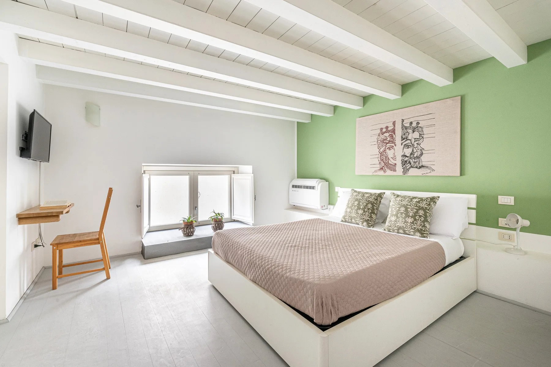 Un dormitorio con una cama grande, una pared verde y vigas blancas en el techo.