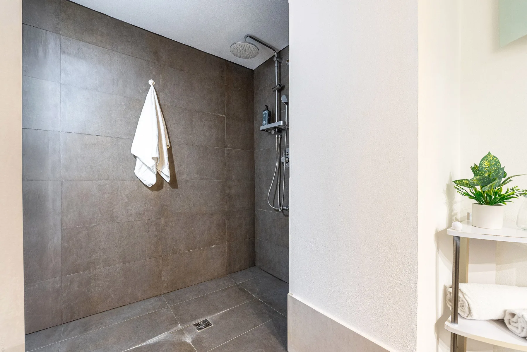 Zona de ducha de un baño con azulejos y una toalla colgada en la pared.