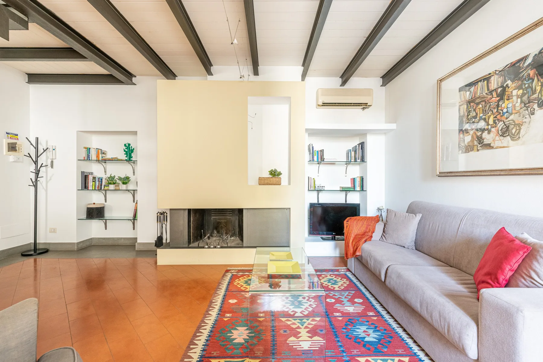 Una sala de estar con un sofá gris, una alfombra colorida y una chimenea.
