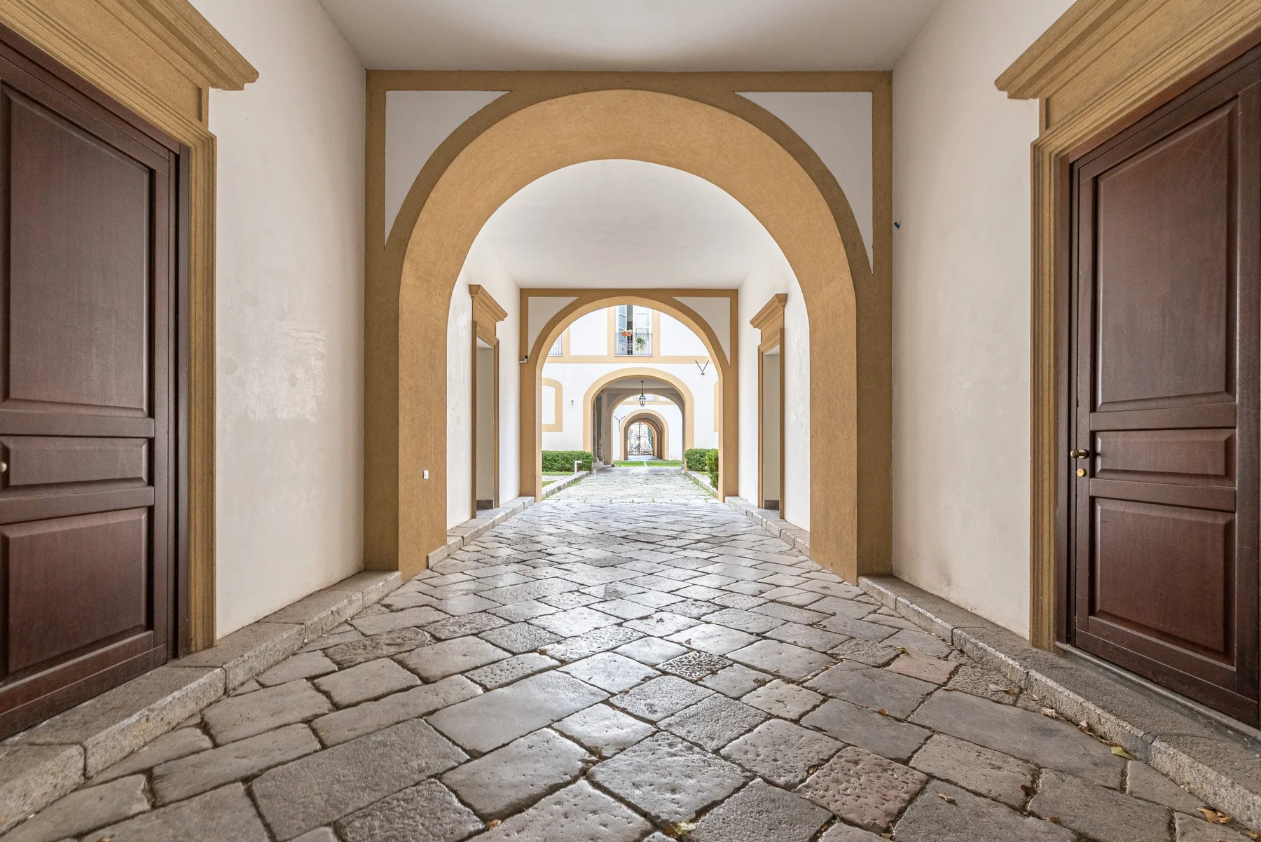 Un pasillo con arcos, pavimento de piedra y puertas de madera oscura.