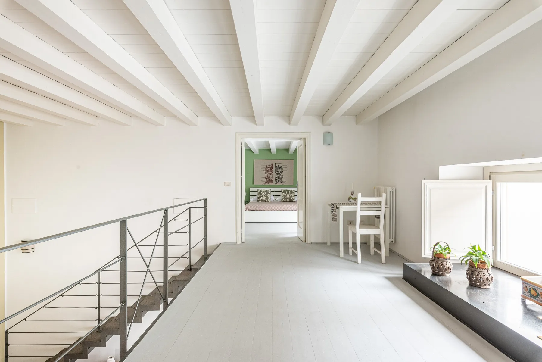 Un interior luminoso tipo loft con vigas expuestas y una barandilla junto a la escalera.