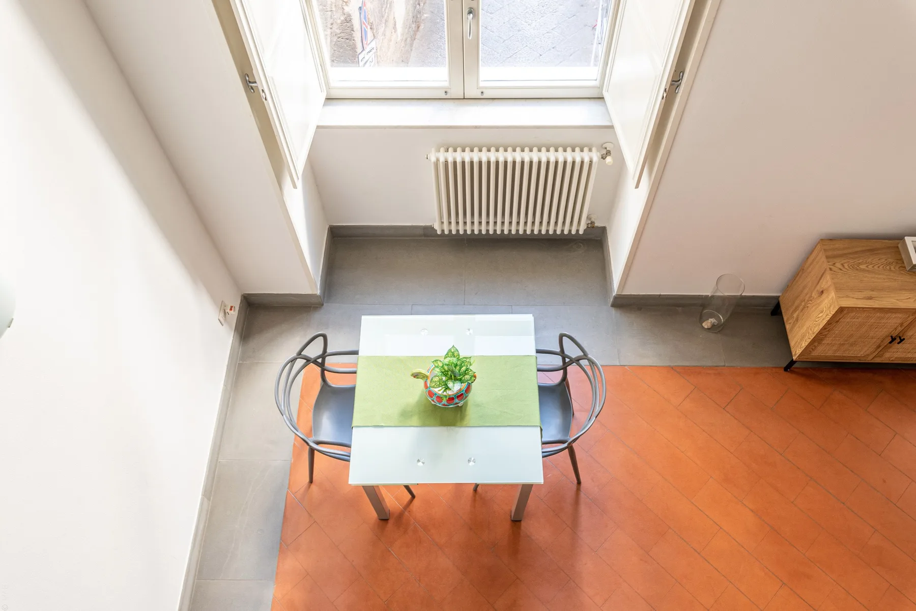 Una pequeña zona de comedor con mesa, sillas y una planta junto a una ventana.
