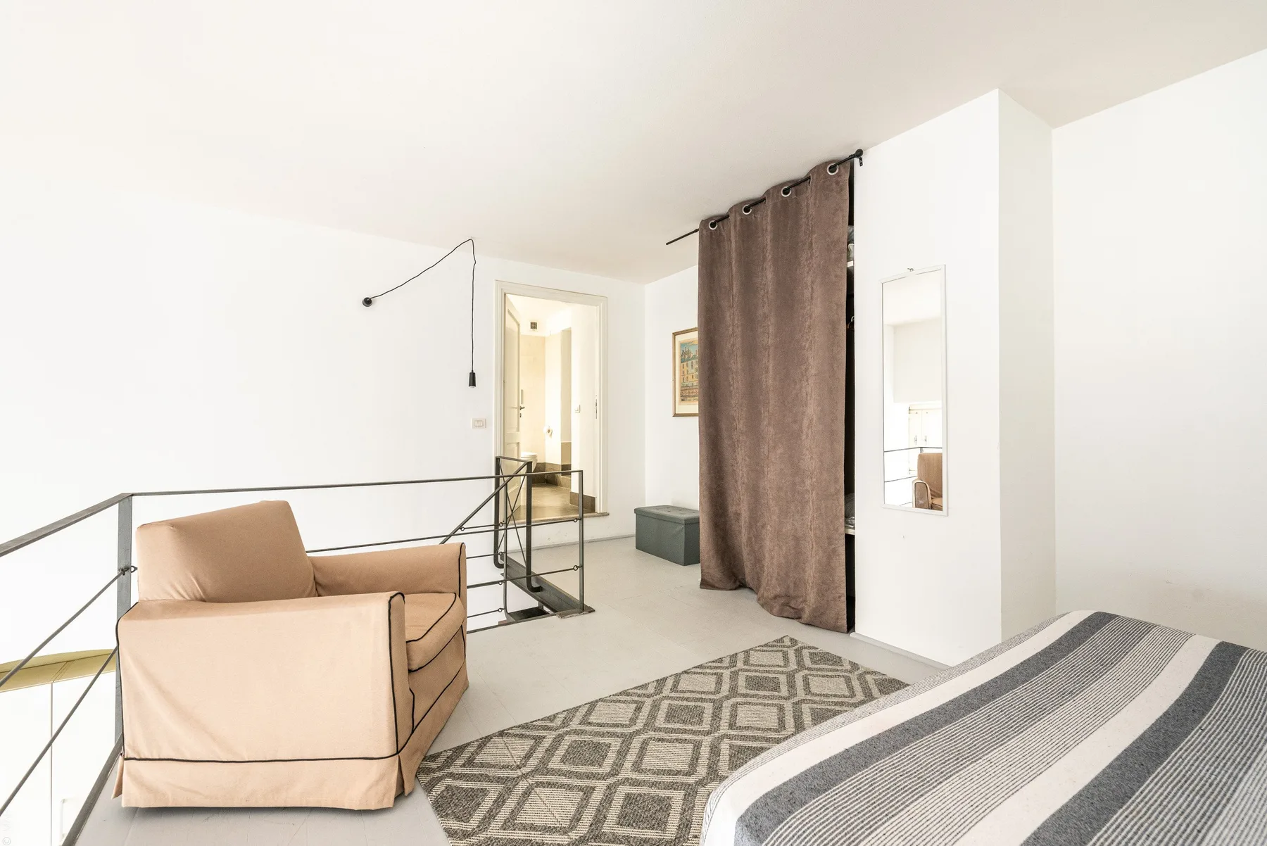 Un dormitorio luminoso con una cama, un sillón y una entrada con cortina.