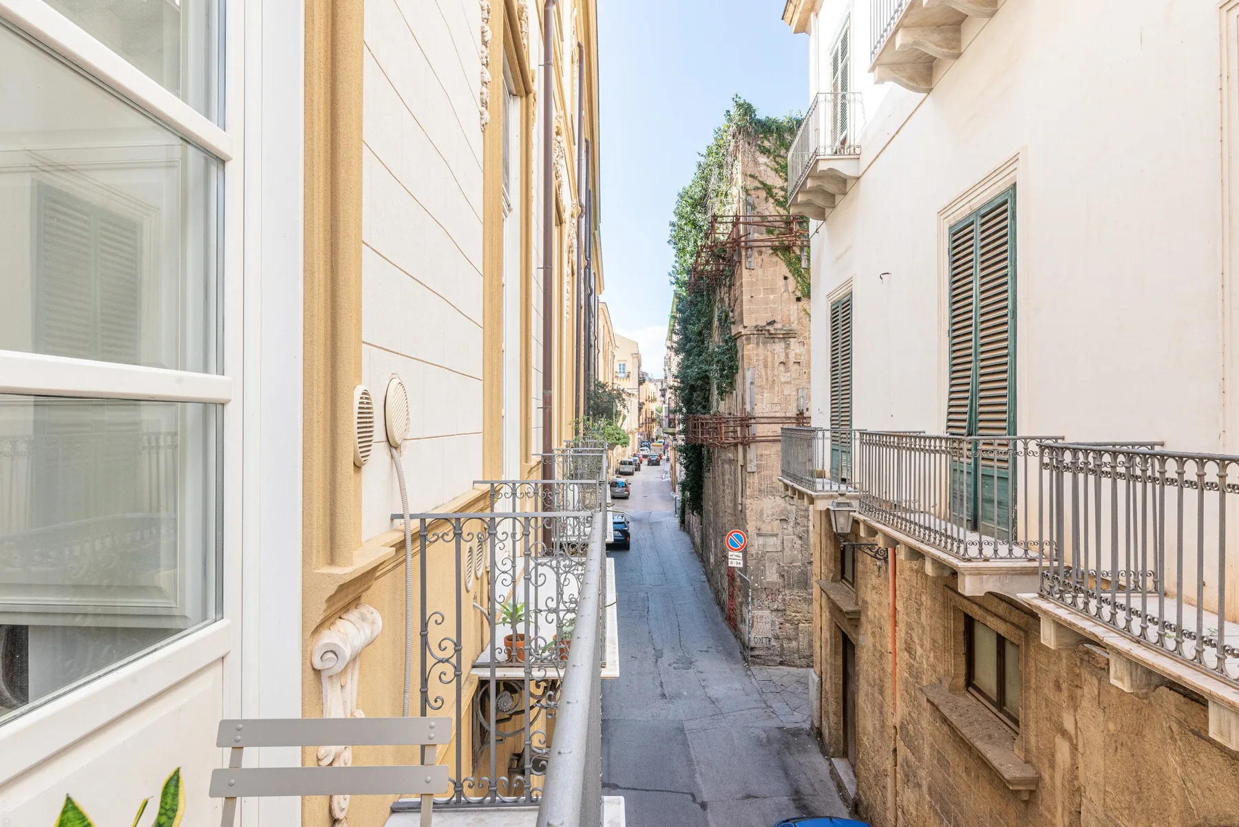 Una calle estrecha pasa entre edificios cercanos con balcones y ventanas con persianas.