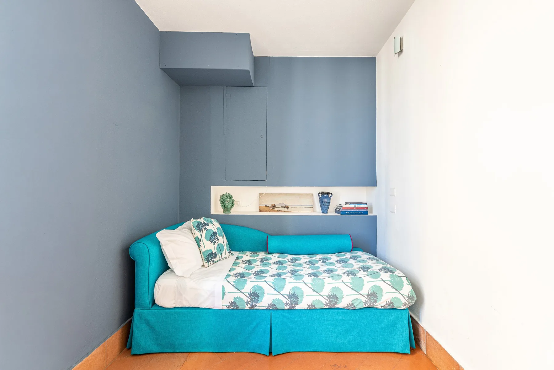 Un dormitorio pequeño con una cama turquesa y ropa de cama estampada.