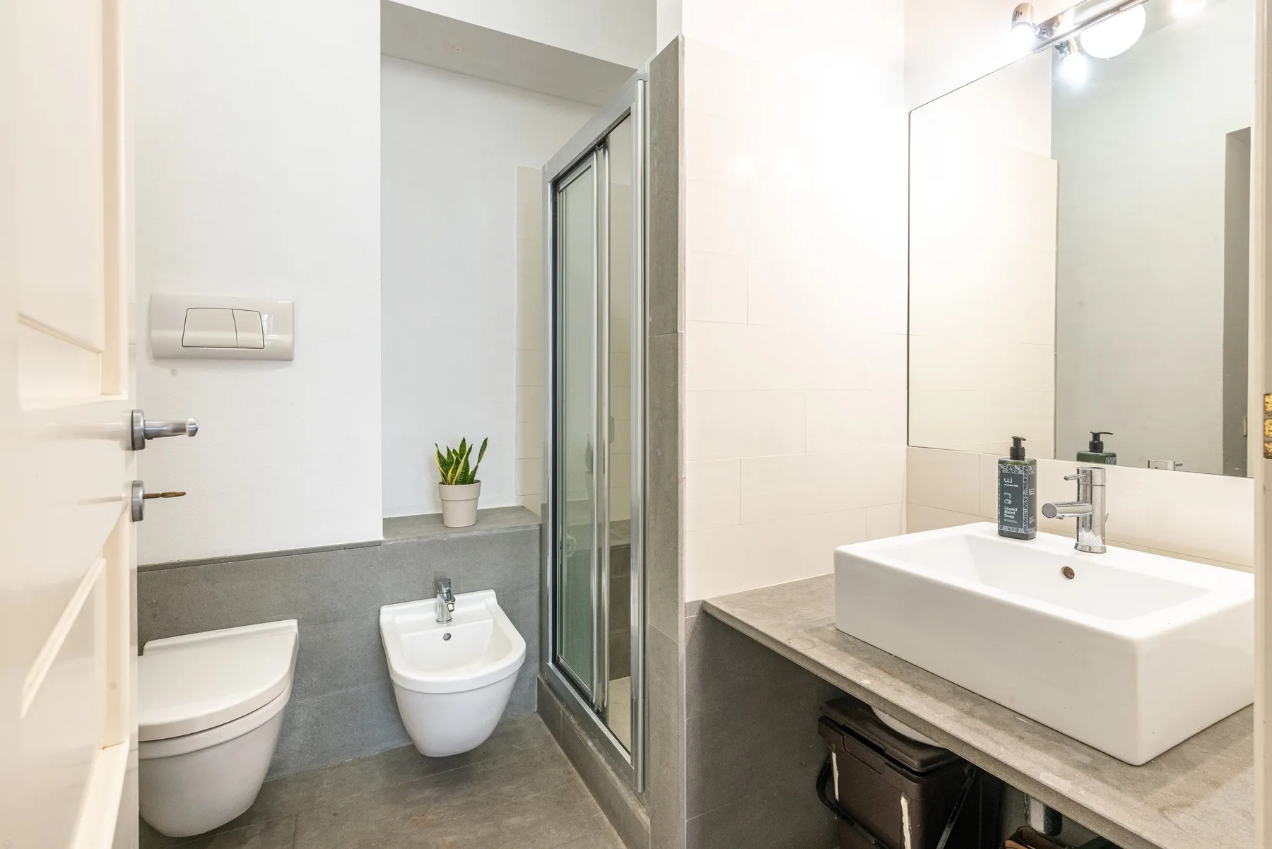Un baño moderno con lavabo, espejo, inodoro y ducha de vidrio.