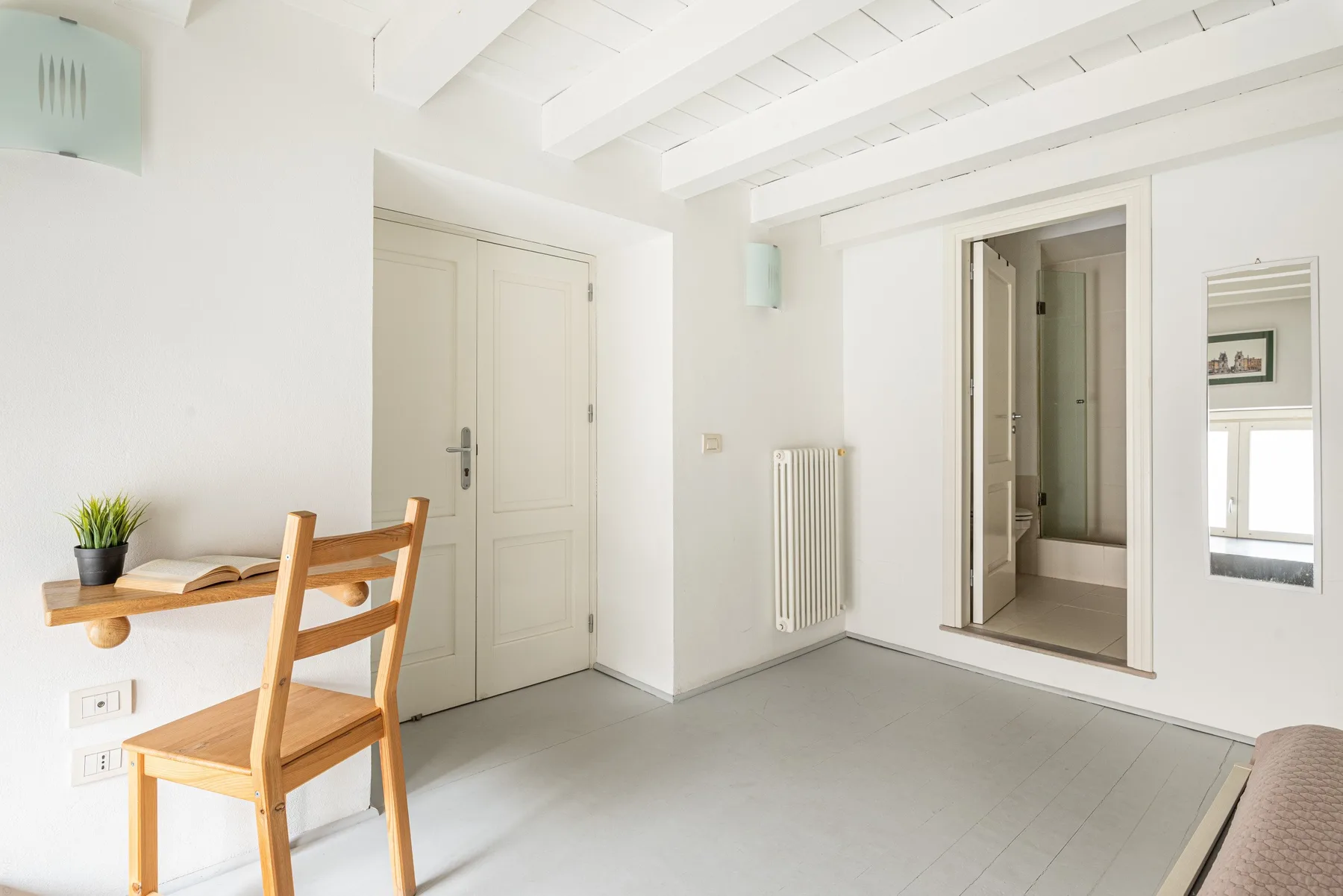 Una habitación luminosa con una silla de madera, un estante y una puerta abierta.
