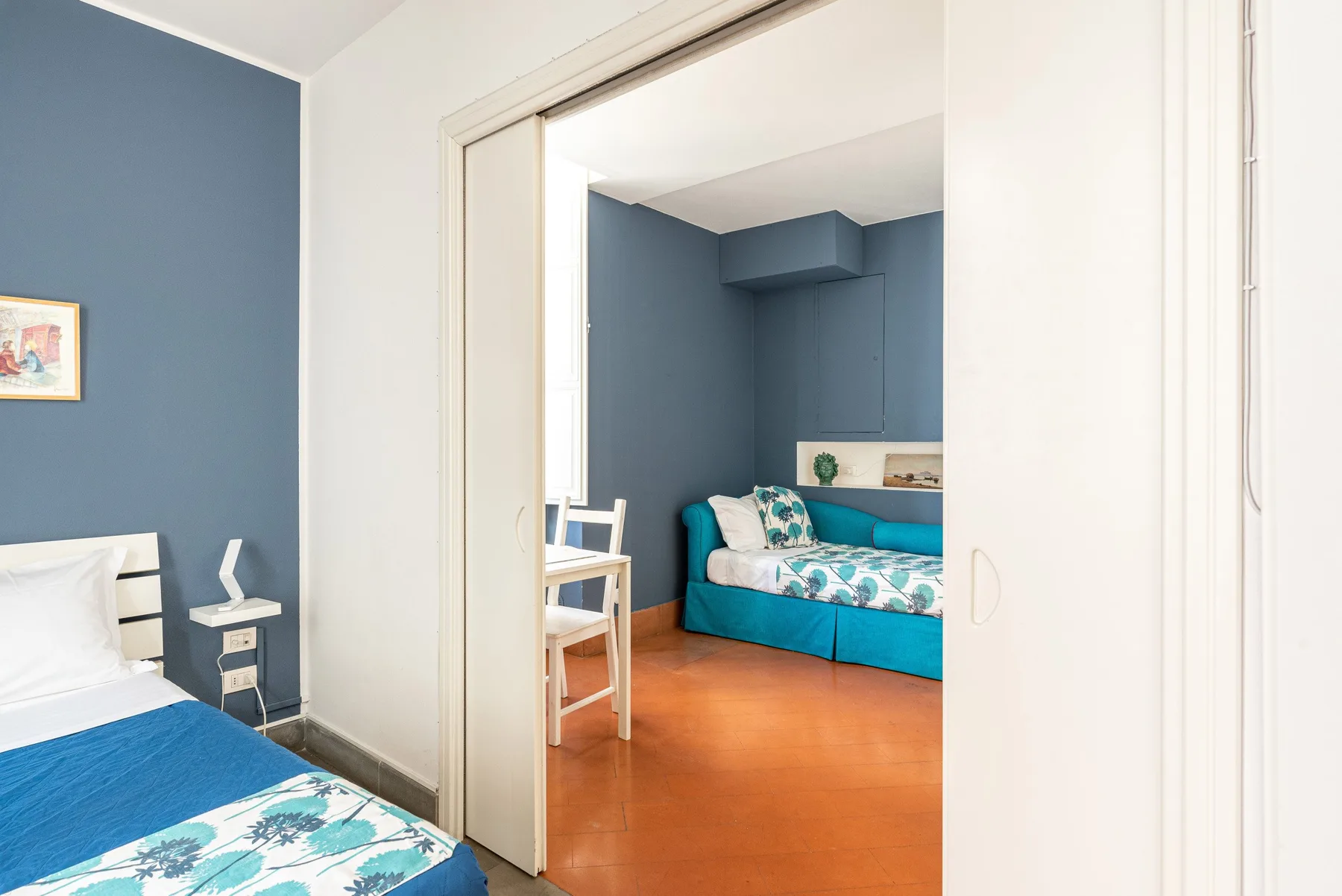 Un dormitorio se abre a una zona de estar con paredes azules y un diván turquesa.
