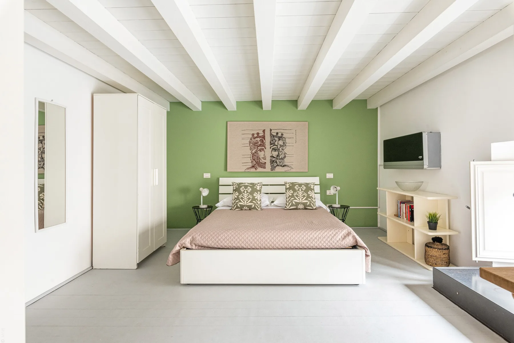 Un dormitorio con una cama frente a una pared verde y vigas blancas en el techo.