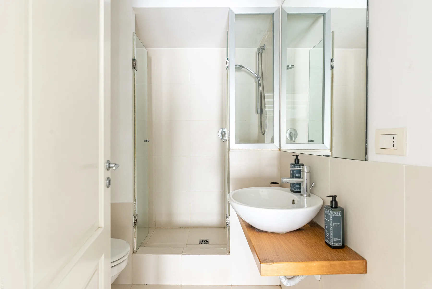 Un baño luminoso con una ducha de vidrio y un lavabo sobre un mueble de madera.