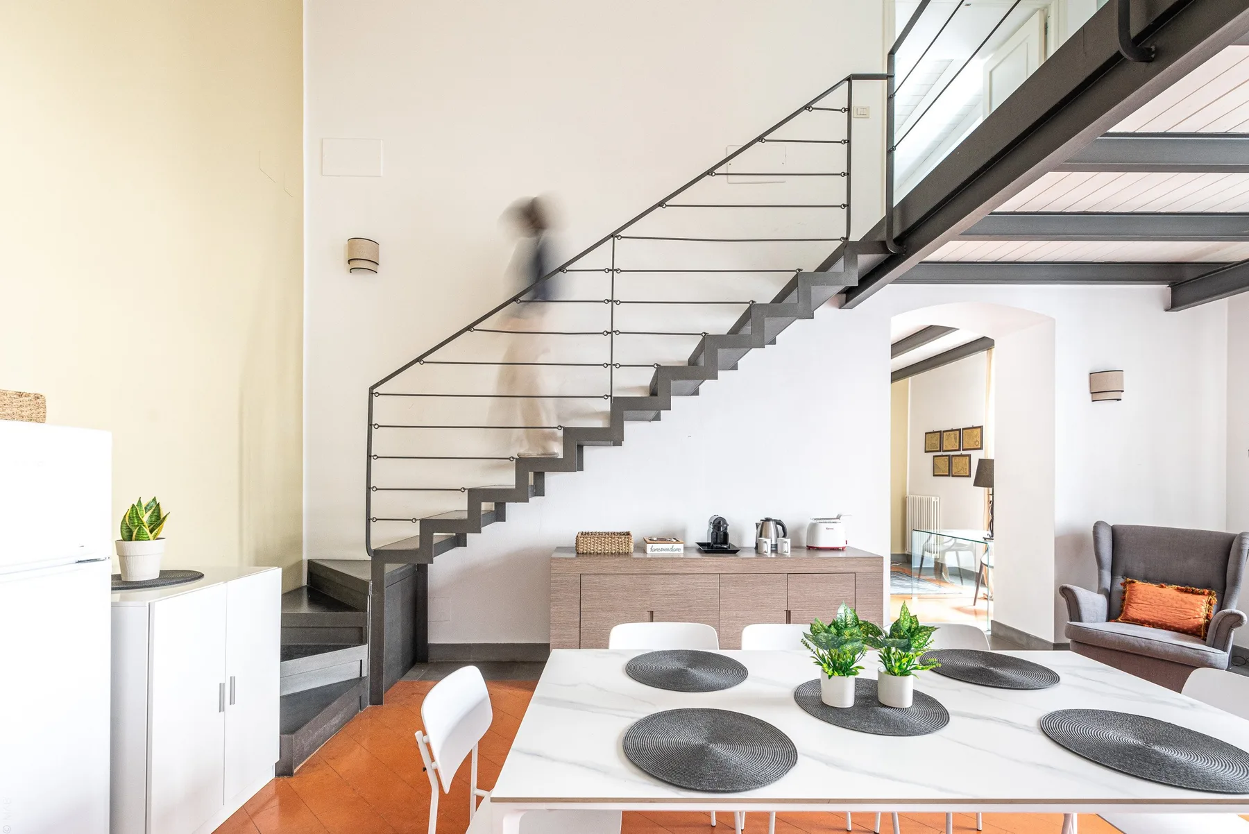 Una luminosa zona de comedor bajo una escalera, con una mesa preparada para comer.