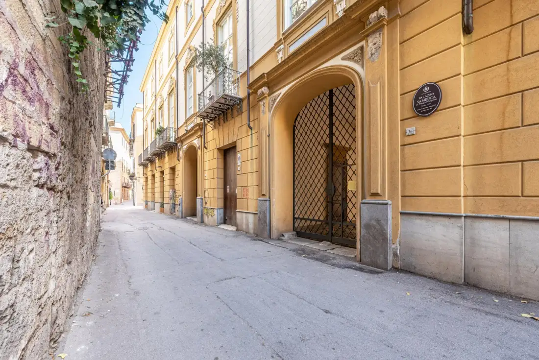Una calle estrecha pavimentada pasa entre un muro de piedra y un edificio amarillo.