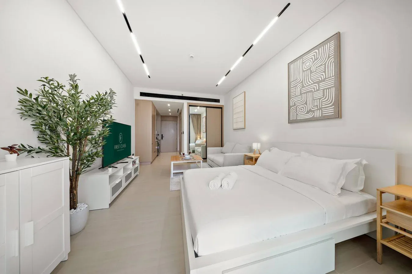 Un dormitorio tipo estudio luminoso con una cama grande, una zona de estar y un televisor.