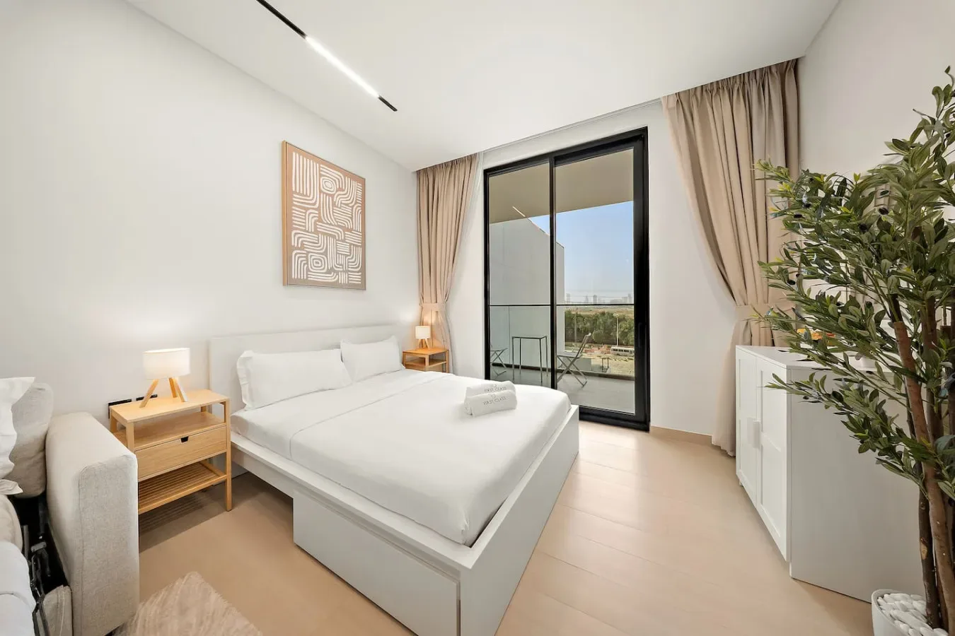 Dormitorio luminoso con una cama blanca junto a puertas de vidrio que dan a un balcón.
