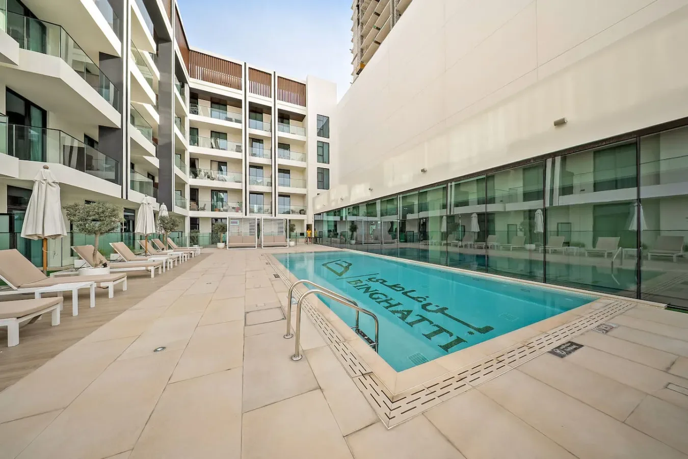 Una piscina al aire libre está rodeada de edificios modernos, con tumbonas junto a la terraza.