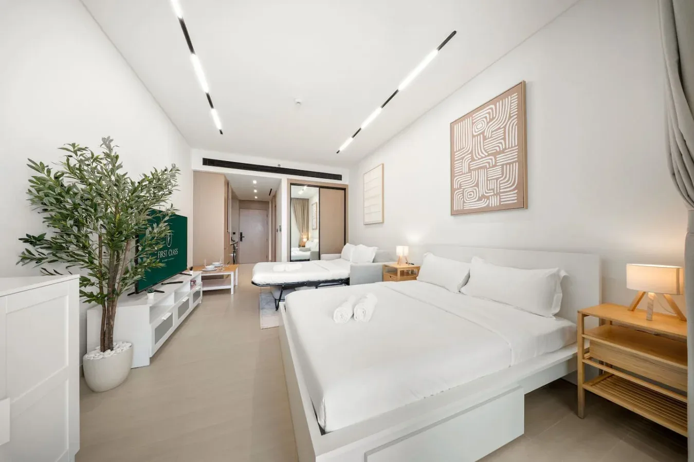Un dormitorio luminoso con una cama grande, una zona de estar y una planta en maceta.