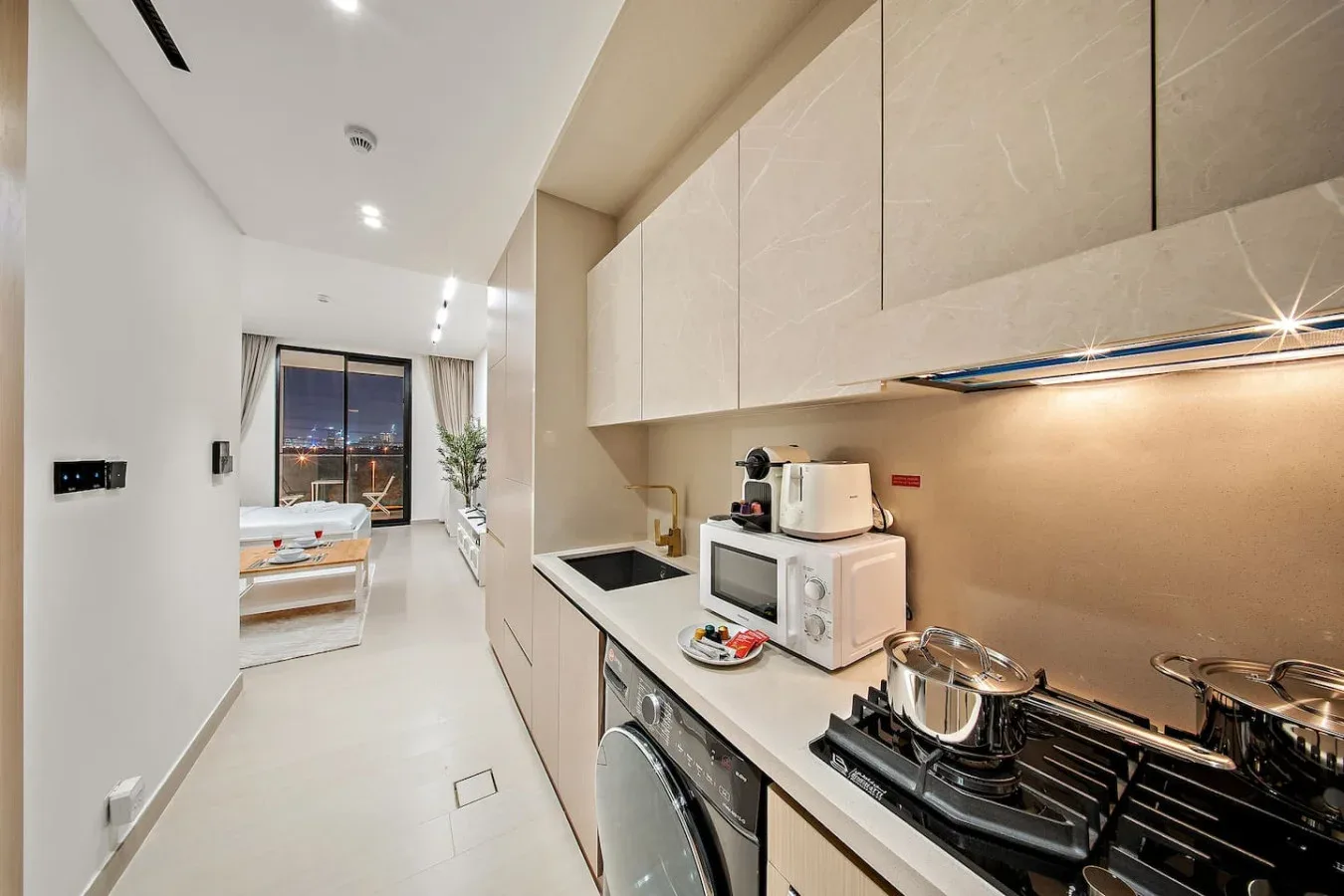 Una cocina moderna de estudio con placa de cocción y electrodomésticos, abierta a una sala de estar.