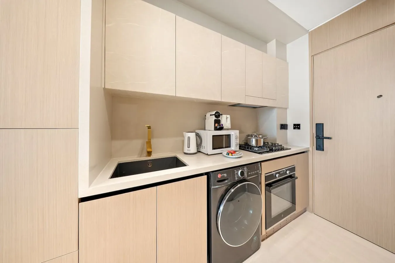 Una cocina compacta con gabinetes claros, una estufa y electrodomésticos integrados.