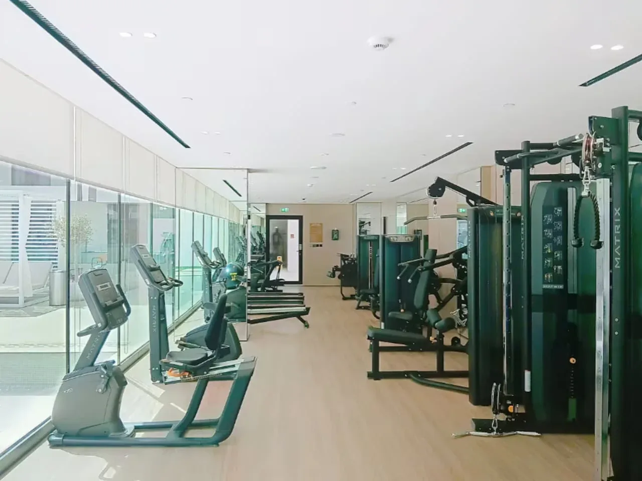 Un gimnasio con máquinas de ejercicio y equipo de entrenamiento junto a las ventanas.