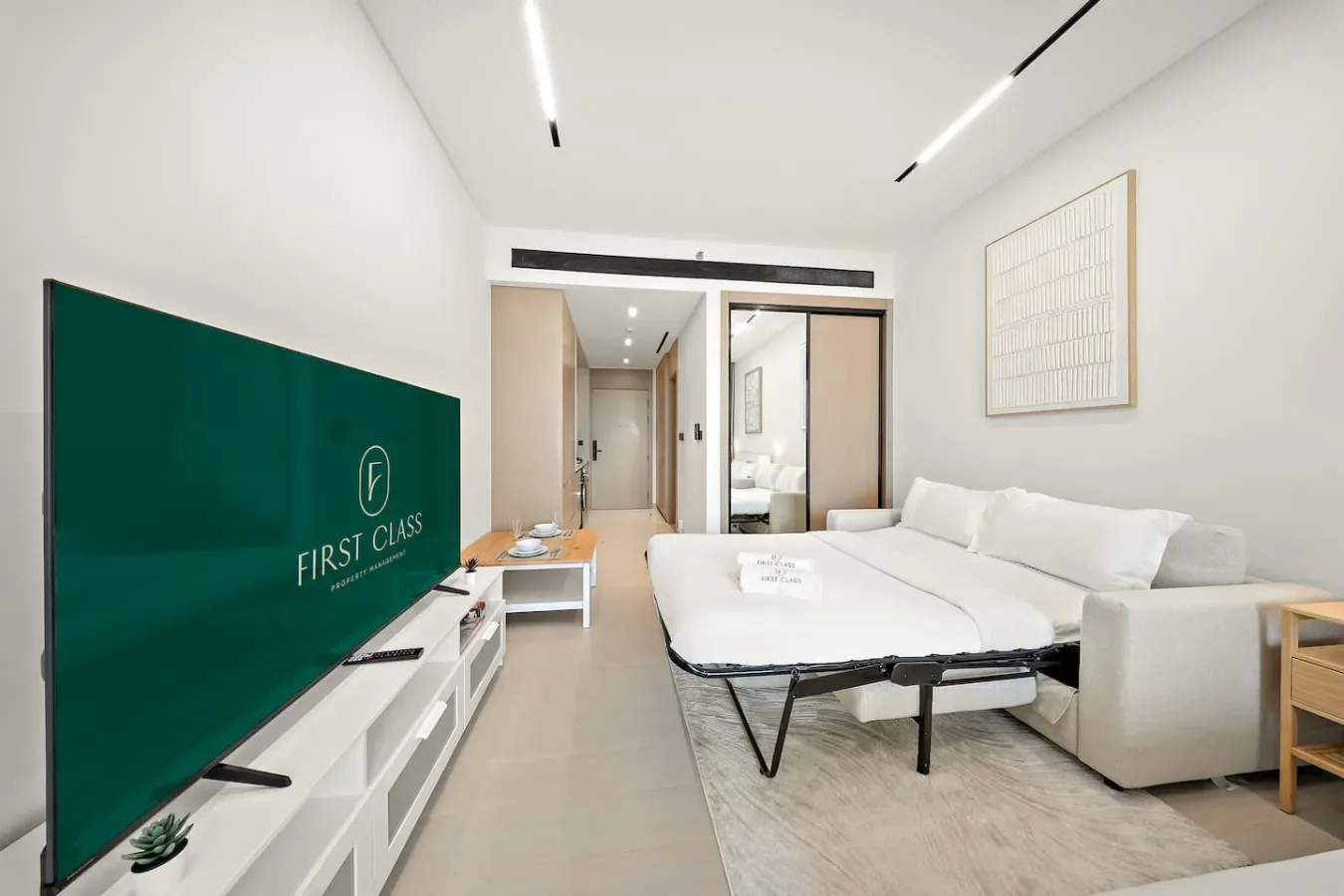 Un dormitorio luminoso con una cama, asientos blancos y un televisor.