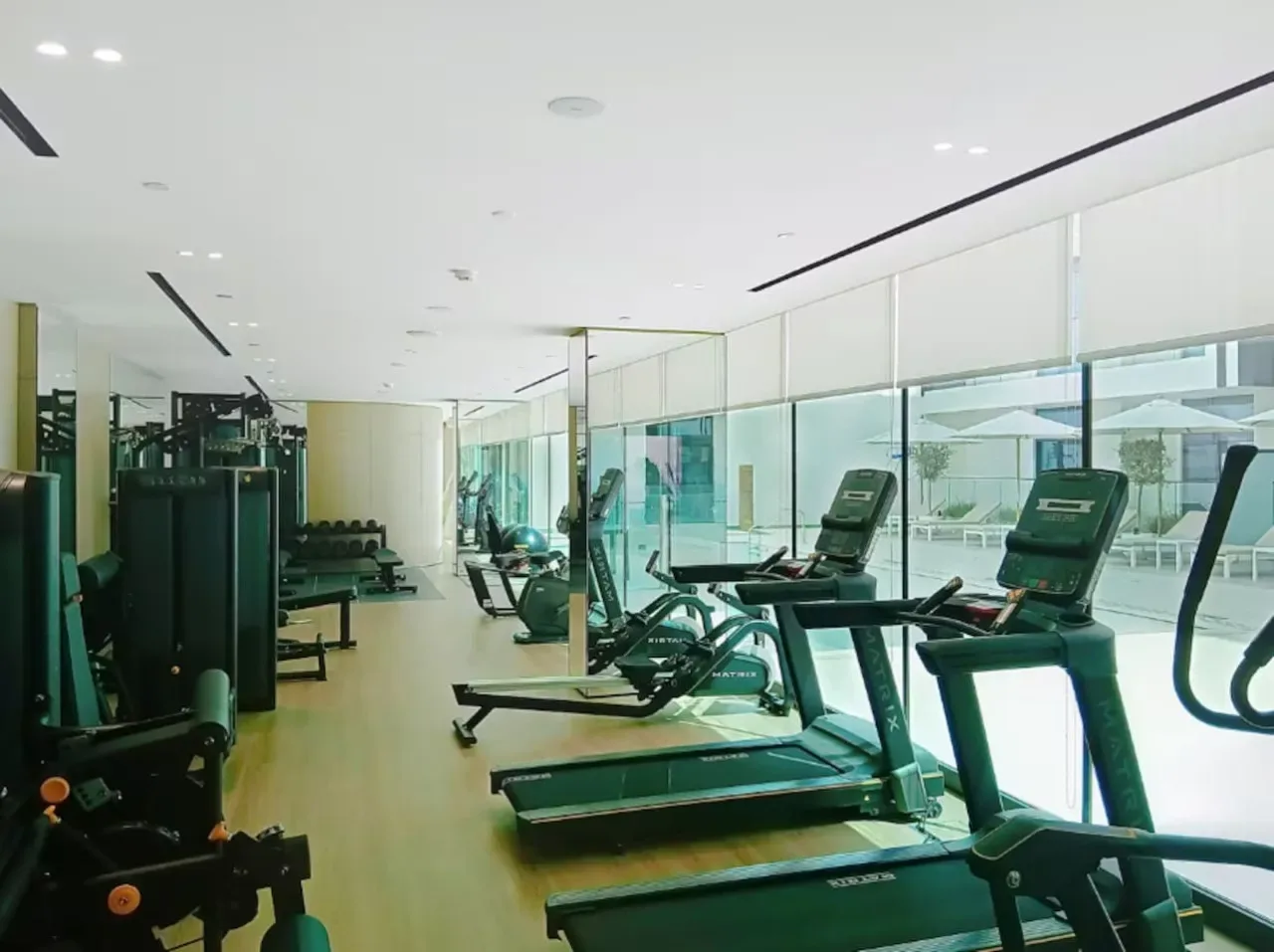 Un gimnasio luminoso con cintas de correr y máquinas de ejercicio junto a grandes ventanales.