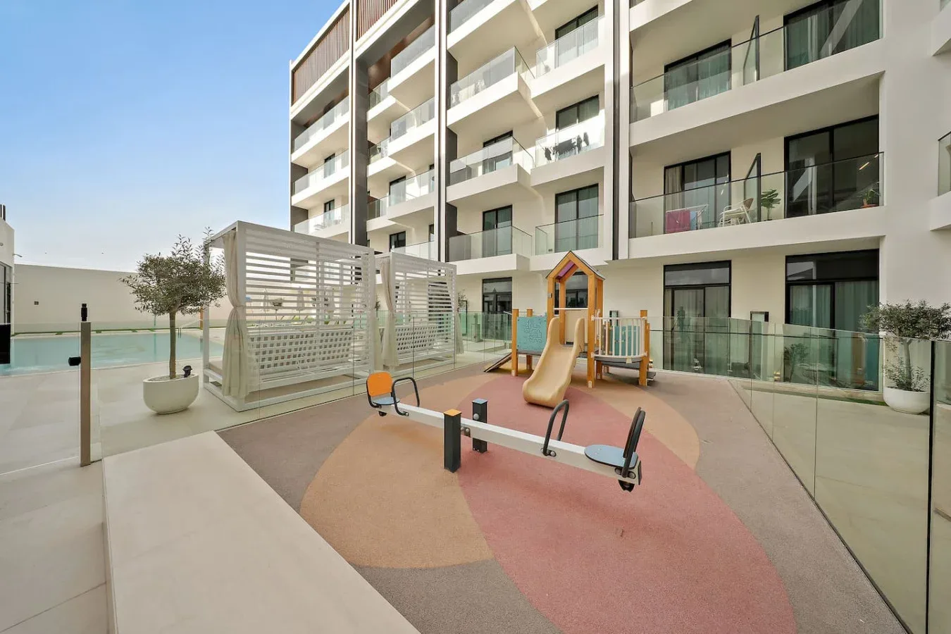 Un parque infantil al aire libre con toboganes y un balancín junto a un edificio moderno.
