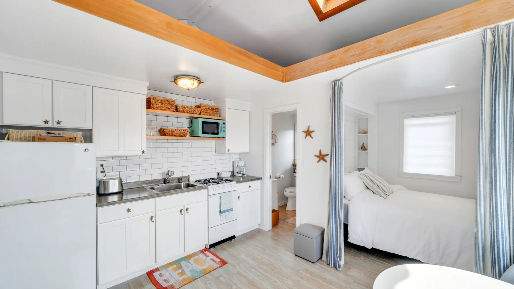 Una pequeña cocina luminosa se abre a una cama junto a una ventana.