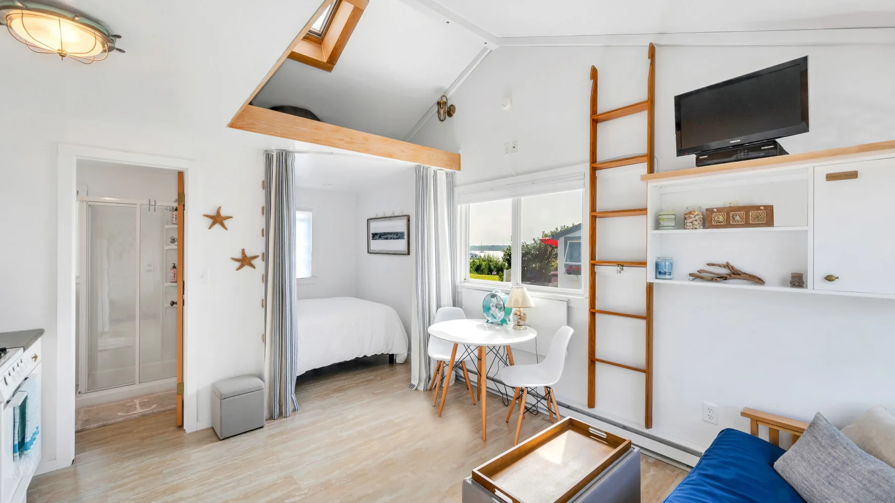 Un dormitorio tipo loft luminoso con cama, mesa de comedor y una escalera junto a estantes empotrados.