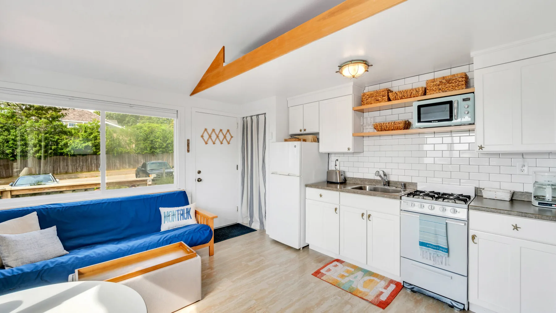 Una luminosa sala de estar da a una cocina compacta, con un sofá azul junto a las ventanas.