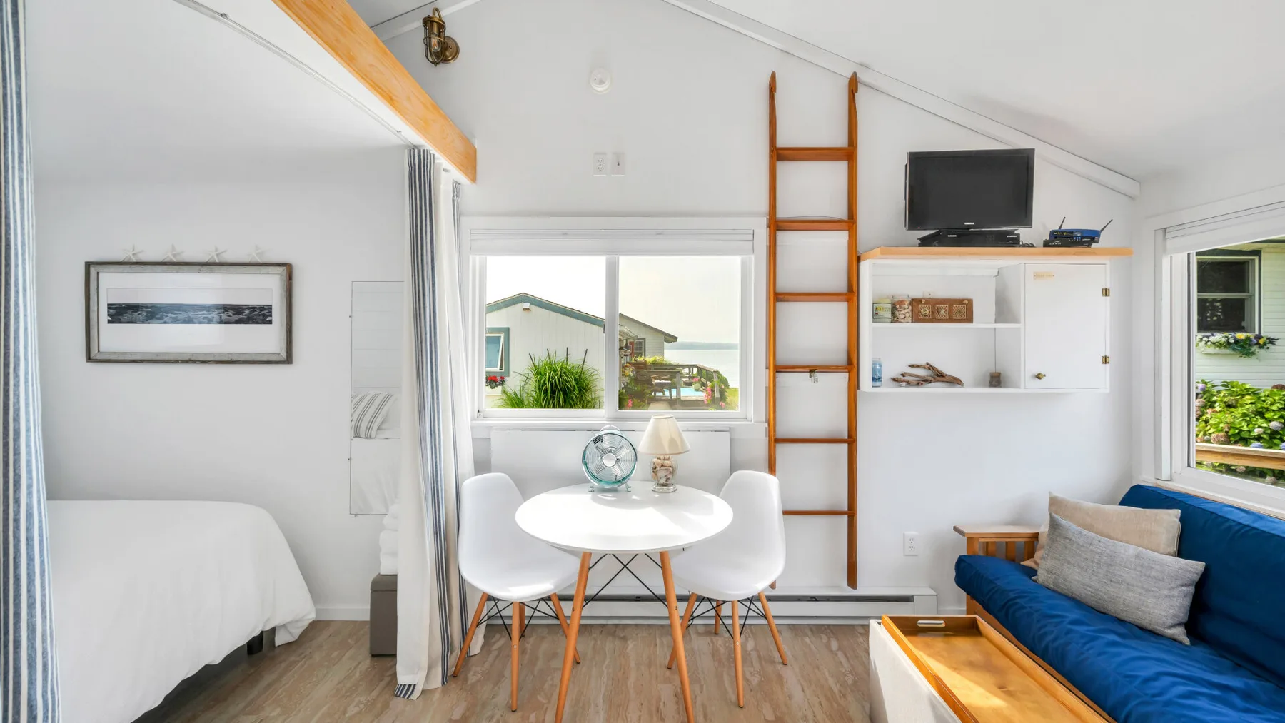 Un dormitorio abuhardillado luminoso con una cama blanca, una mesa y asientos azules.
