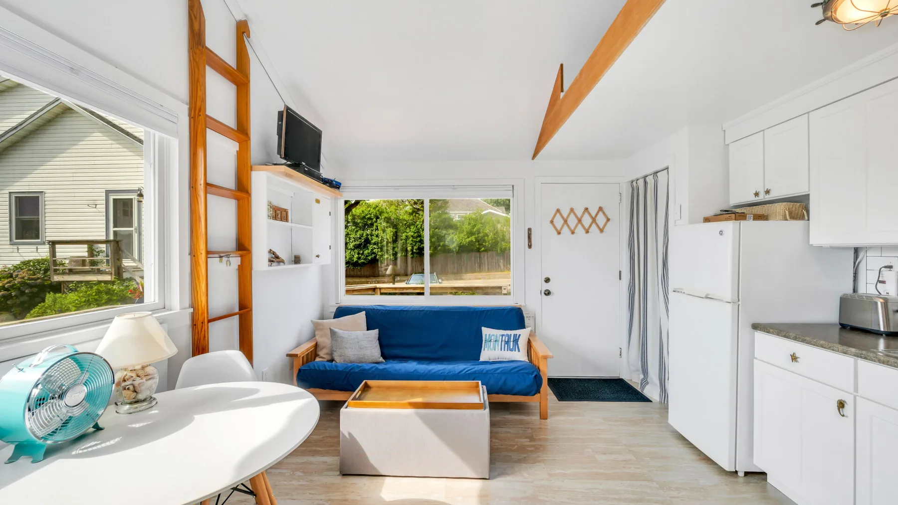 Una luminosa sala de estar con asientos azules, una mesa blanca y grandes ventanas.