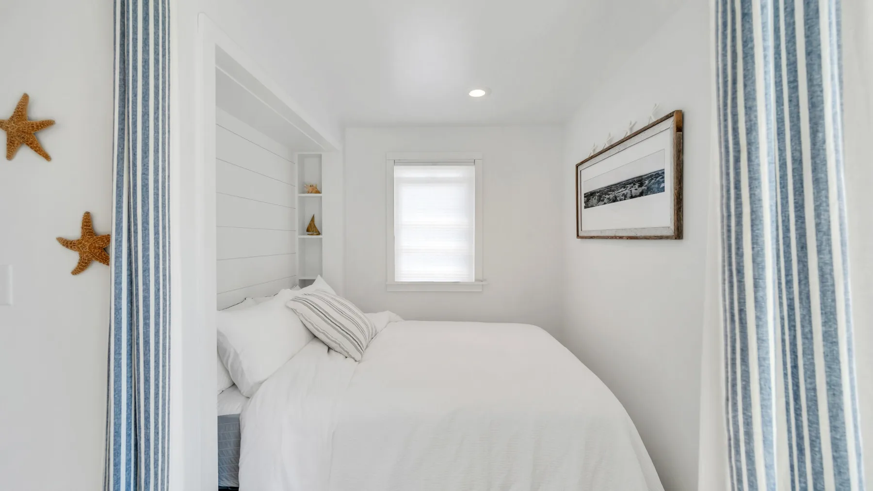 Un dormitorio luminoso con una cama blanca y cortinas a rayas.